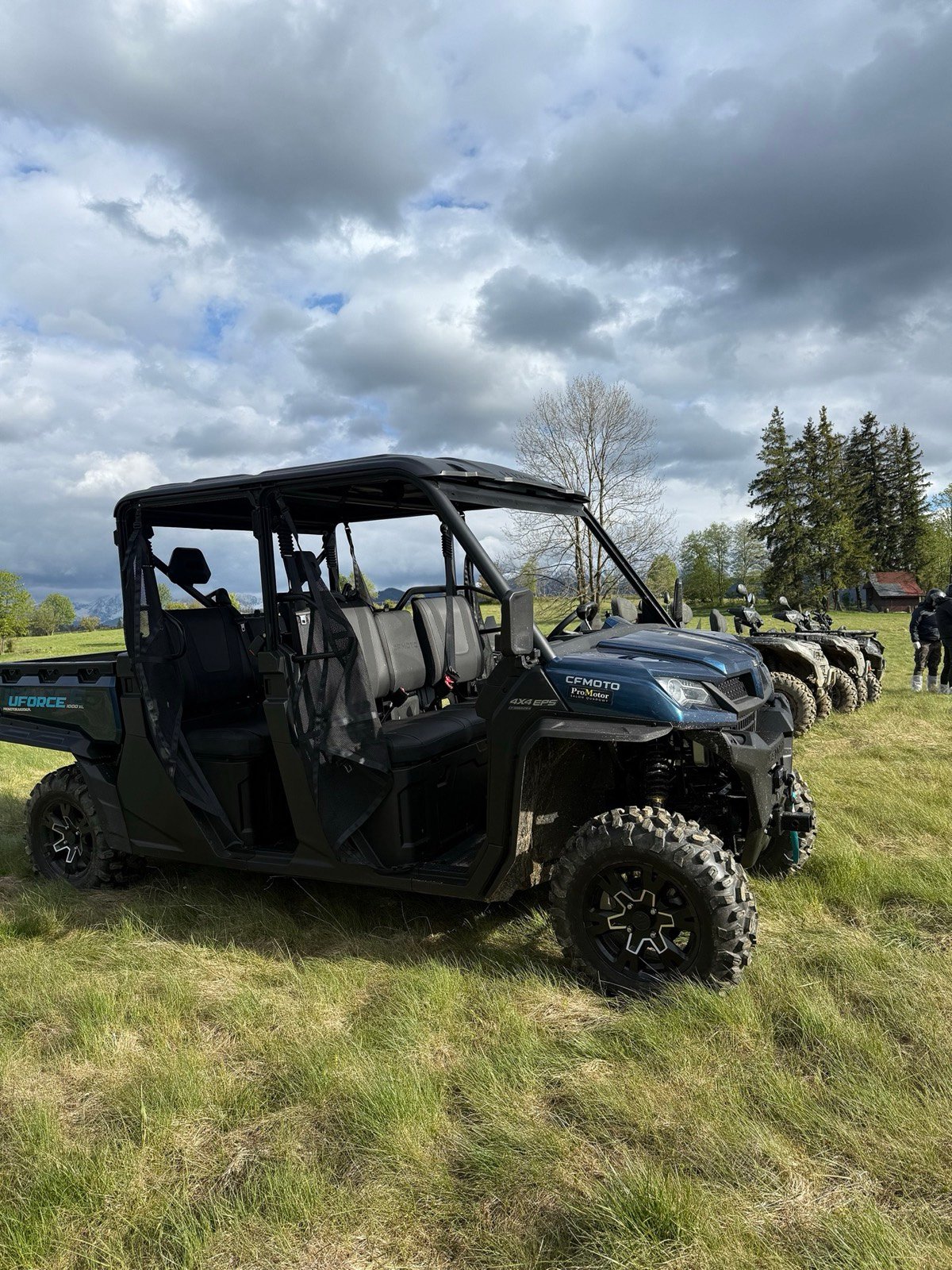 Sześcioosobowe buggy CFMoto z dwoma rzędami siedzeń na łące, obok quady