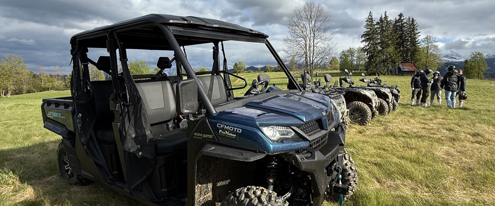Sześcioosobowe buggy na łące, obok quady i grupa, w tle chmury nad górami