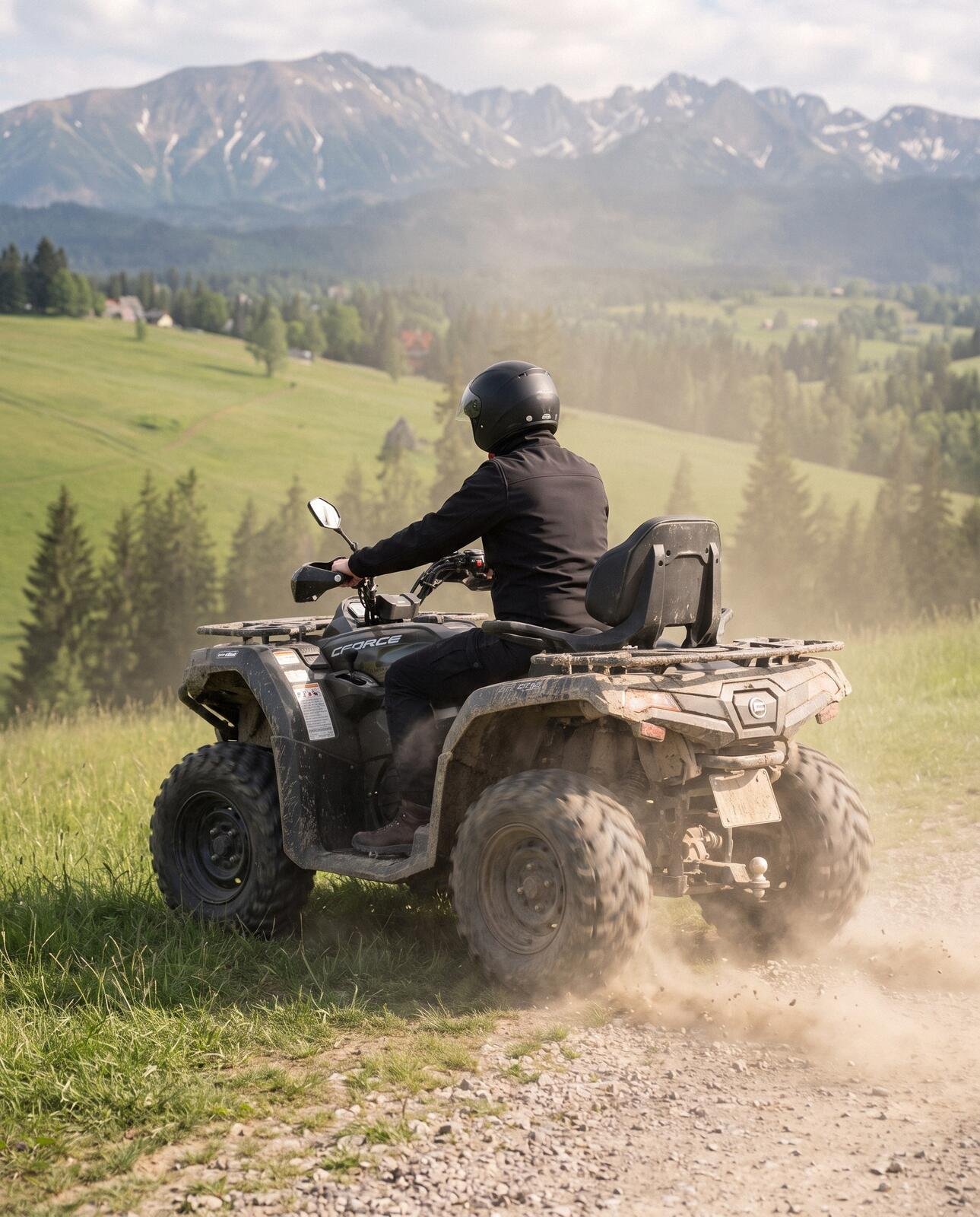 Quad widziany z tyłu wzbija kurz na trawiastym zakręcie, przed nim hale, świerki i Tatry