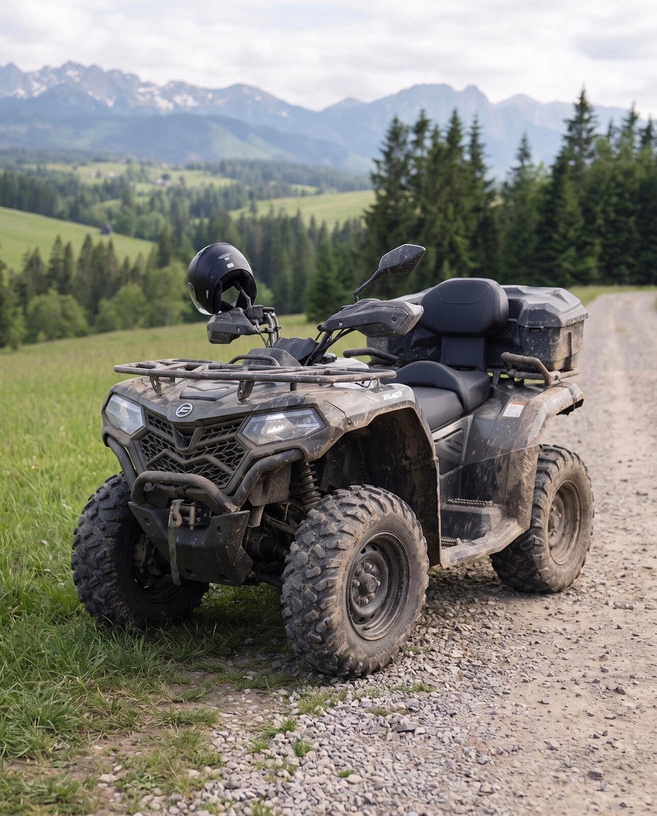 Zabłocony dwuosobowy quad z kaskiem na lusterku stoi na szutrowej drodze wśród świerków, w tle Tatry
