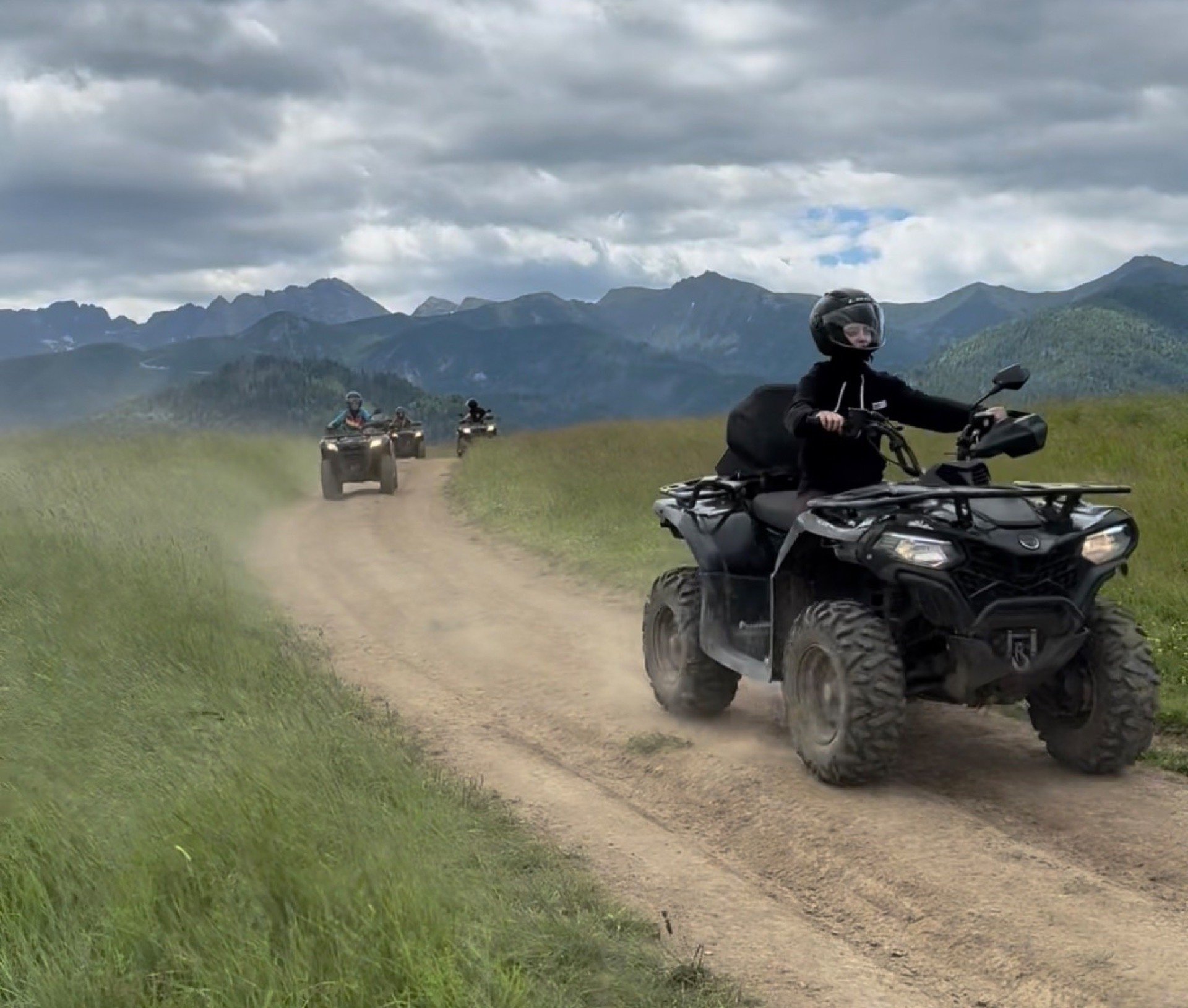 Quad w chmurze kurzu na polnej drodze, za nim kolejne, na horyzoncie pasmo Tatr