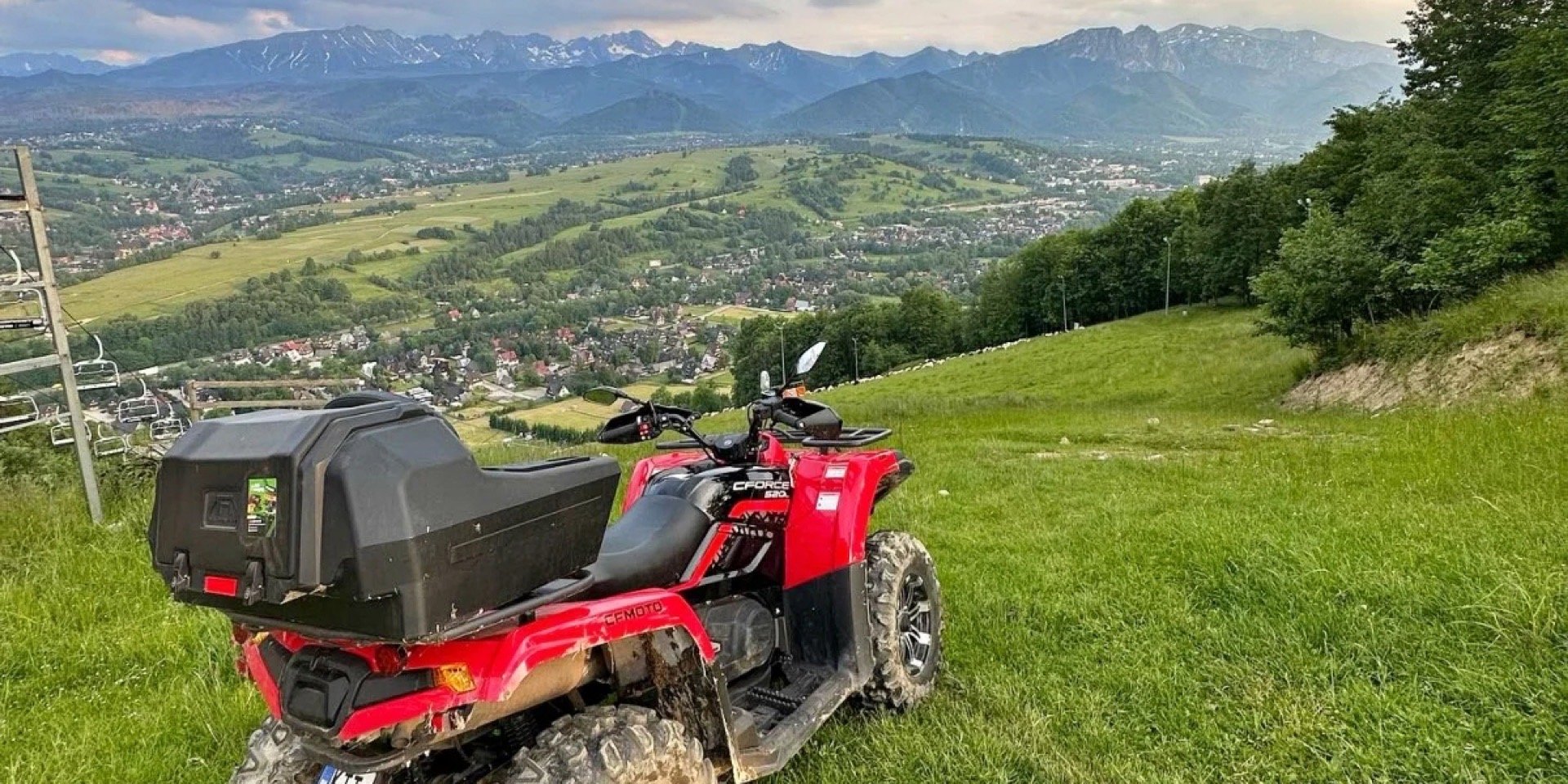 Czerwony quad na zboczu nad Zakopanem, w dole miasto, w tle grzbiet Tatr